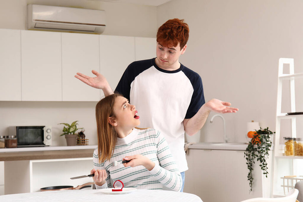 Young man proposing to his displeased girlfriend in kitchen - Fotó, kép
