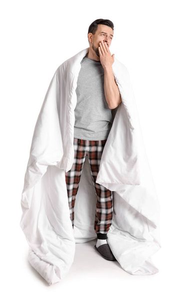 Bonito homem com cobertor macio bocejando no fundo branco - Foto, Imagem