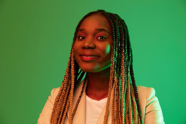 African american woman portrait business smile on green background in neon light, color mixed light, bright colors. Beauty African American woman with pigtails emotions. High quality photo - Photo, Image