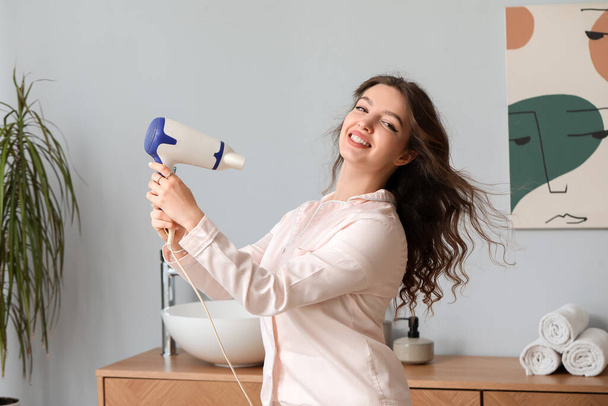 Pretty young woman with hair dryer in bathroom - Fotó, kép