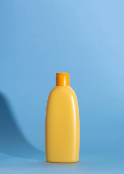 Asse de uma garrafa amarela com cosméticos de crianças em um contexto azul. Sombras duras, espaço de cópia. - Foto, Imagem