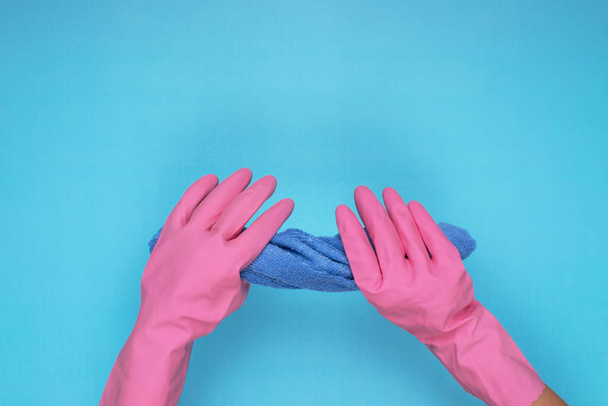 femme portant des gants de nettoyage rose sur fond bleu clair, tenant une lingette de nettoyage - Photo, image