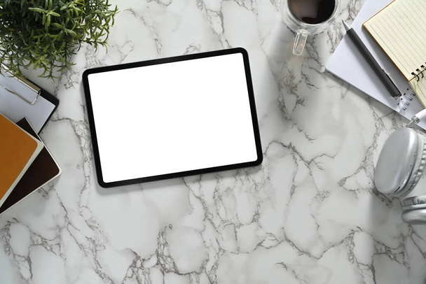 Vue du dessus de la tablette numérique avec écran blanc vide, casque et tasse à café sur fond de marbre. - Photo, image