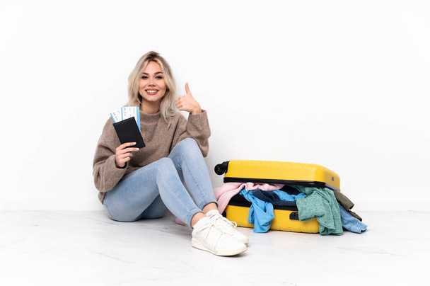 Подростковая блондинка с чемоданом, набитым одеждой, сидящей на полу, показывая знак "хорошо" и жест "вверх". - Фото, изображение