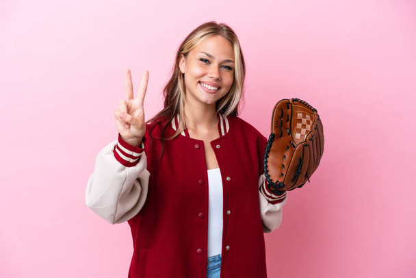 Player Russian woman with baseball glove isolated on pink background smiling and showing victory sign - Foto, imagen
