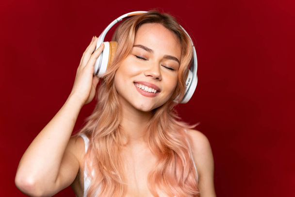 tiener meisje met roze haar luisteren muziek over geïsoleerde rode achtergrond - Foto, afbeelding