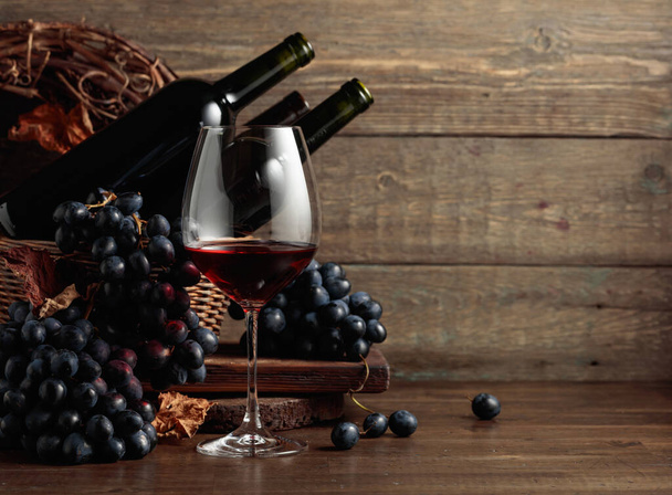 Red wine and blue grapes. Wine and grapes in a vintage setting on an old wooden table. - Photo, image
