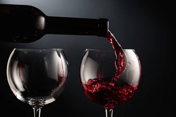 Наливание красного вина в бокал вина на черном фоне. - Фото, изображение