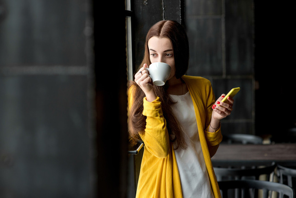 Vrouw met telefoon en een kopje koffie - Foto, afbeelding