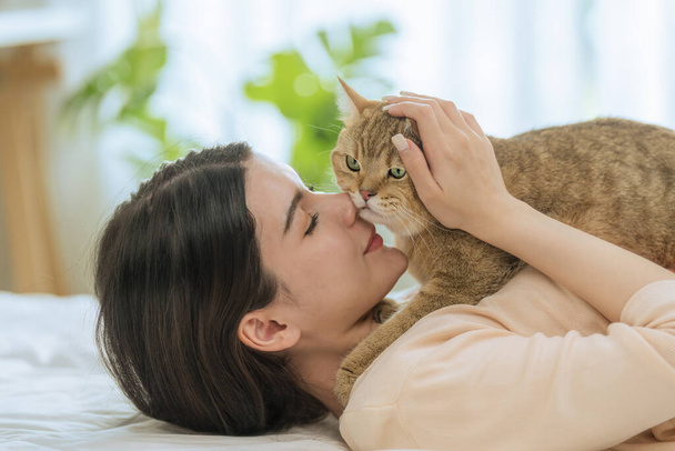 A lovely snapshot showcasing a beautiful young Asian woman lying on her bed in the morning, playfully kissing her adorable cat. This sweet interaction takes place in a warm, sunlit bedroom setting - Photo, Image