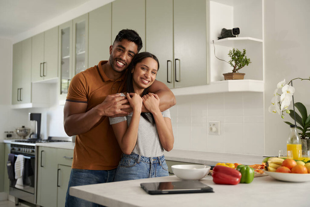 Šťastný mladý biracial pár s úsměvem a objímání vedle jídla a digitální tablet v kuchyni - Fotografie, Obrázek