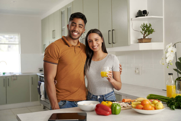 Young biracial couple wearing casual clothing smiling and looking at camera by food in kitchen - Фото, изображение