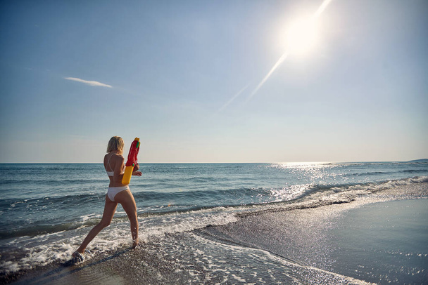Young attractive woman with water gun walking on beach. Beautiful woman on summer vacation. Holiday, fun, lifestyle concept. - Foto, Bild