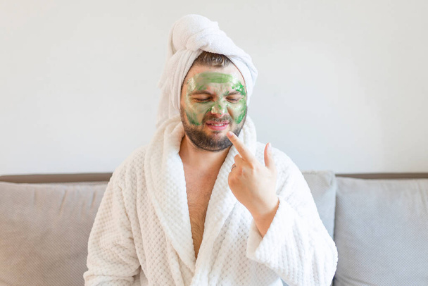 Lustiger bärtiger Mann trägt grüne Maske zur Hautpflege auf.  - Foto, Bild