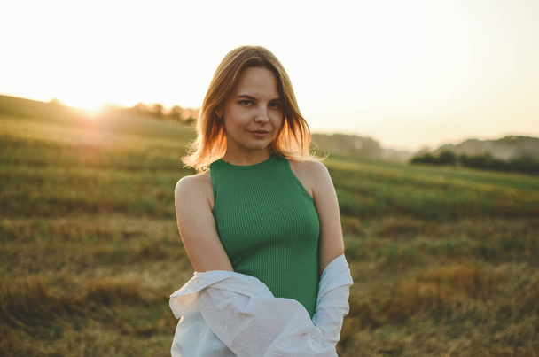 a girl in a green dress stands on the background of the sunset.Photo of a girl in a field at sunset.Atmospheric photo in a field in sunlight.Blonde with short hair.sensual photo of a girl.delicate portrait.sunset portrait.playful woman.Ukrainian. - Valokuva, kuva