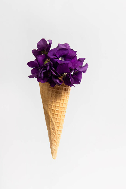 Ice cream cone with wild violets on white background. Spring flowers concept. - Foto, Imagem