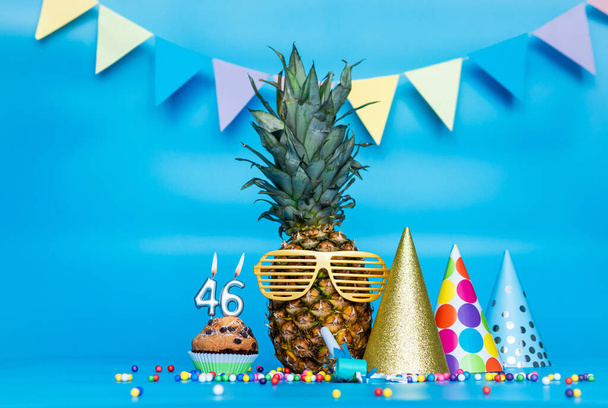 Creative background with pineapple character in sunglasses copy space. Happy birthday background with muffin or cake with candle number  46. Anniversary holiday decorations on a blue background. - Fotó, kép