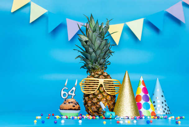 Creative background with pineapple character in sunglasses copy space. Happy birthday background with muffin or cake with candle number  64. Anniversary holiday decorations on a blue background. - Fotó, kép