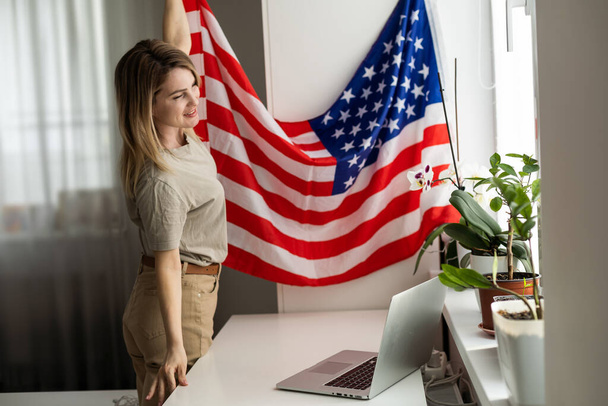 Obrázek šťastné mladé dámy s vlajkou USA pomocí notebooku. Hledá kameru. Kvalitní fotografie - Fotografie, Obrázek