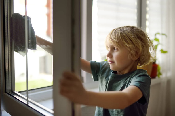 Cute little boy washing a window at home. Child helping parents with household chores, for example, cleaning windows in his house. Children doing housework. Kids household duties - Photo, Image