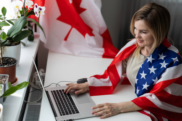 Szczęśliwa kobieta pracownik siedzi zawinięty w flagę USA, krzycząc z radości w miejscu pracy biurowej, świętując dzień pracy lub dzień niepodległości USA. Wysokiej jakości zdjęcie - Zdjęcie, obraz