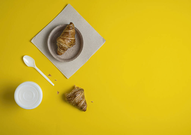 Coffee and croissant on the table, take-away food on a yellow background, a croissant bitten off - Photo, image
