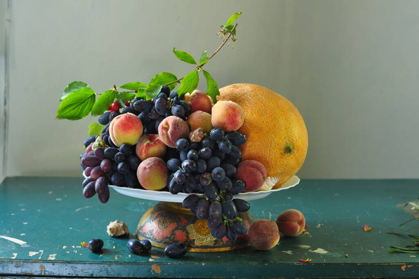 still life with ripe blue grapes and other fruits in a plate on the table - Foto, imagen