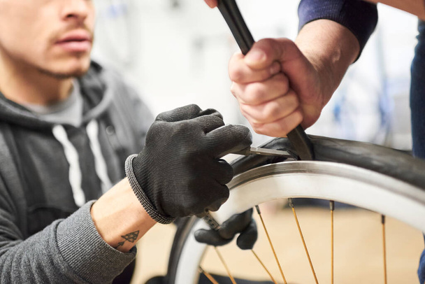 自転車修理工場の自転車の車輪から空気のないタイヤを除去するために協力して働く2人の男性。コピースペース付きの選択フォーカス構成. - 写真・画像