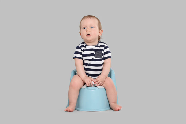 Little child sitting on baby potty against light grey background - Foto, Imagen