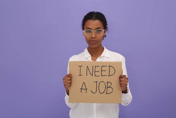 Unemployed African American woman holding sign with phrase I Need A Job on violet background - Fotografie, Obrázek