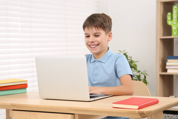 Smiling boy using laptop at desk in room. Home workplace - 写真・画像