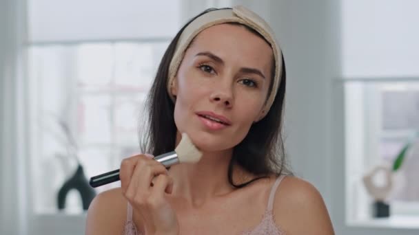 Satisfied girl powdering face using brush at home portrait. Smiling woman posing camera applying makeup with cosmetics in white bathroom closeup. Relaxed lady morning preparations and beauty treatment - Footage, Video