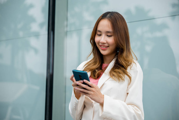Portrait successful business woman smiling holding smartphone use application chat online in morning, Asian businesswoman working with mobile phone standing against street front building near office - Foto, imagen