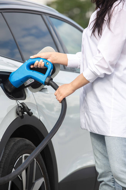 Young business woman refueling her electric car at a EV charging station. Concept of environmentally friendly vehicle. Electric car concept. Green travelling. - Photo, Image