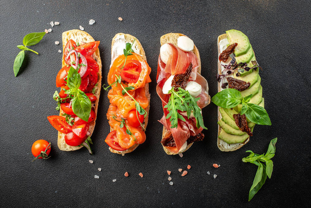 a set of bruschetta with prosciutto, salmon, tomatoes and avocado on a wooden board, banner, menu, recipe place for text, top view, - Photo, image
