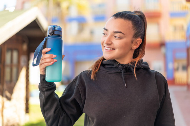 Jeune jolie femme sportive avec une bouteille d'eau à l'extérieur avec une expression heureuse - Photo, image