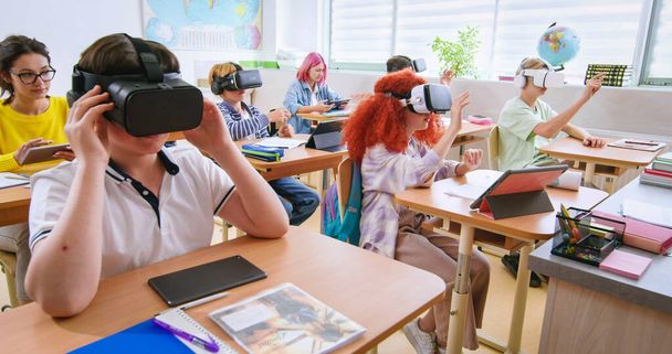Smart pupils wearing VR headsets and studying with future technologies at classroom. Excited boys and girls in virtual glasses experienced augmented reality at lesson in school. - Photo, image