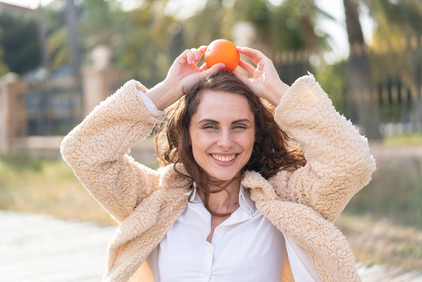 Młoda biała kobieta na świeżym powietrzu trzymająca pomarańczę - Zdjęcie, obraz