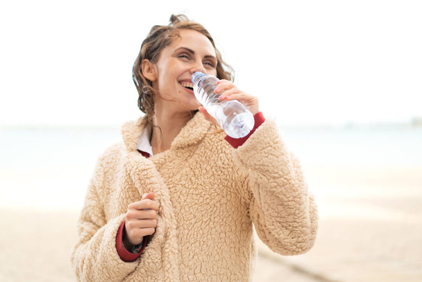 屋外で水のボトルを持つ若い白人女性 - 写真・画像