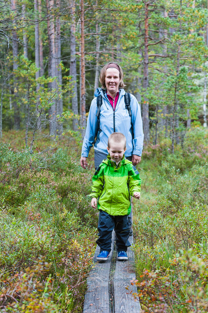 A young boy and his mother enjoy a leisurely hike in the wilderness, surrounded by lush green trees and abundant plant growth. - Photo, Image