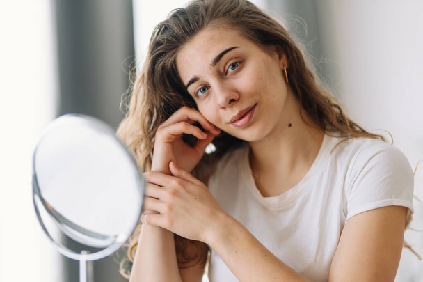 Beautiful  woman with problem skin looking into mirror. Dermatology. Allergic reaction from cosmetic, red spot or rash on face. Beauty care from skin problem. - Zdjęcie, obraz