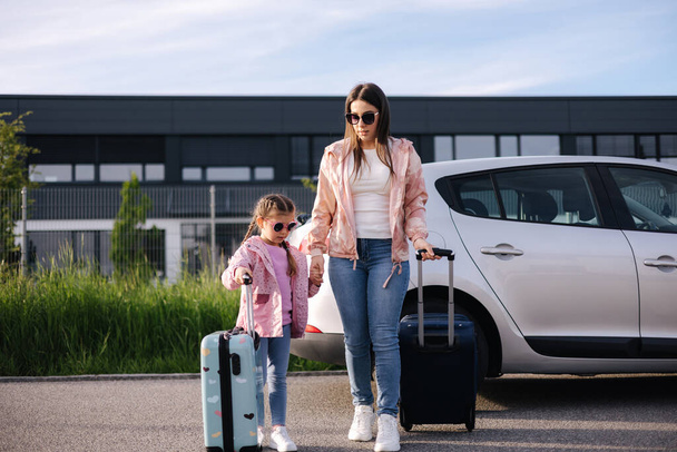 お母さんとの愛らしい娘はスーツケースを持って空港へ行きます。二人の女の子が旅行に行く。女の子は母親と一緒に旅行する。高品質の写真 - 写真・画像