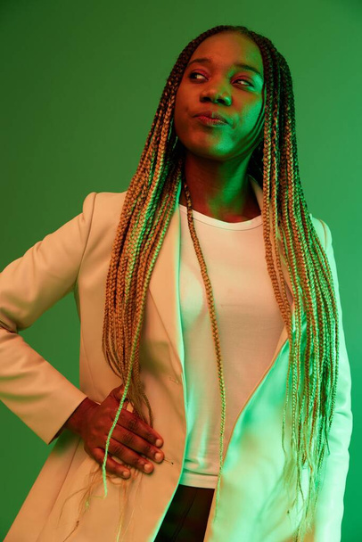 Afrikanische amerikanische Frau Portrait Business Lächeln auf grünem Hintergrund in Neonlicht, Farbe gemischtes Licht, helle Farben. Schönheit afroamerikanische Frau mit Zöpfen Emotionen. Hochwertiges Foto - Foto, Bild