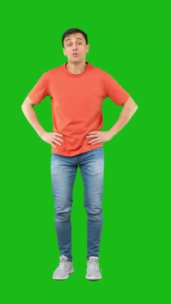 Full body of shocked male covering mouth with hand and looking at camera while standing with hand on waist isolated on green background - Materiał filmowy, wideo