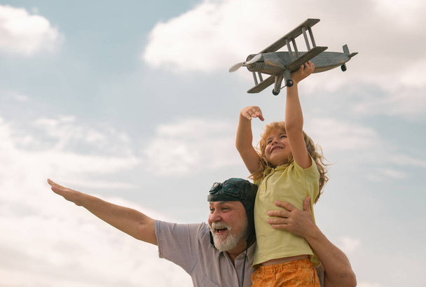 Excited child boy and grandfather having fun with plane outdoor on sky background with copy space. Child dreams of flying, happy childhood with grand dad - Foto, Imagen