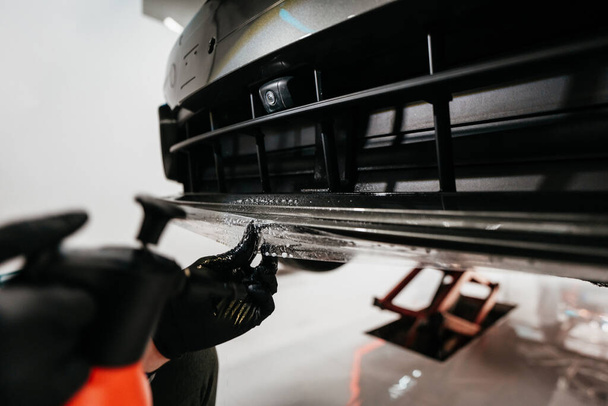 Professional vehicle detailing service in a modern car workshop. Car workshop specialist putting vinyl foil or film on car. Worker using steam pistol for better wrapping and tightening foil edges.  - Φωτογραφία, εικόνα