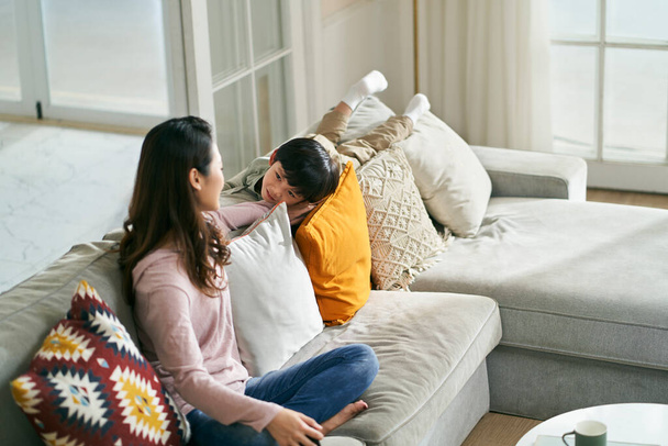 young asian woman mother sitting on family couch keeping company with five-year-old son - Fotografie, Obrázek