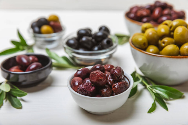 Set of green, red and black olives on a white background. Various types of olives in bowls and olive oil with fresh olive leaves. Delicacy.Mediterranean Kitchen. Copy space. - Photo, Image