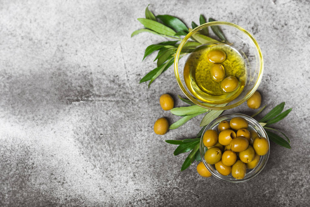 Green olives in a bowl with olive oil and leaves on a textured marble backdrop. Delicious and healthy food. Delicacy.Mediterranean Kitchen. Close-up. Place for text. copyspace. - Fotografie, Obrázek