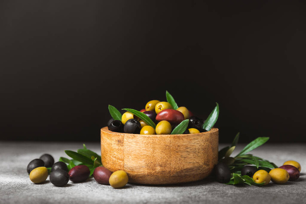A set of green, red and black olives on a black marble background. Different types of olives in bowls and olive oil with fresh olive leaves. Delicacy.Mediterranean Kitchen. Copy space. - 写真・画像